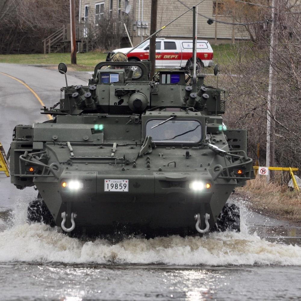 Un blindé roule sur une route inondée.