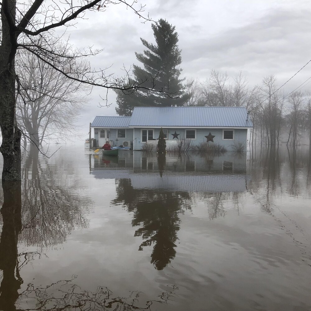 Une femme en canot devant une maison inondée à Maugerville, au Nouveau-Brunswick.