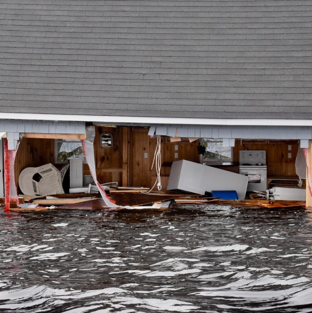 Vue de l'intérieur d'une habitation inondée dont un mur est presque complètement arraché.