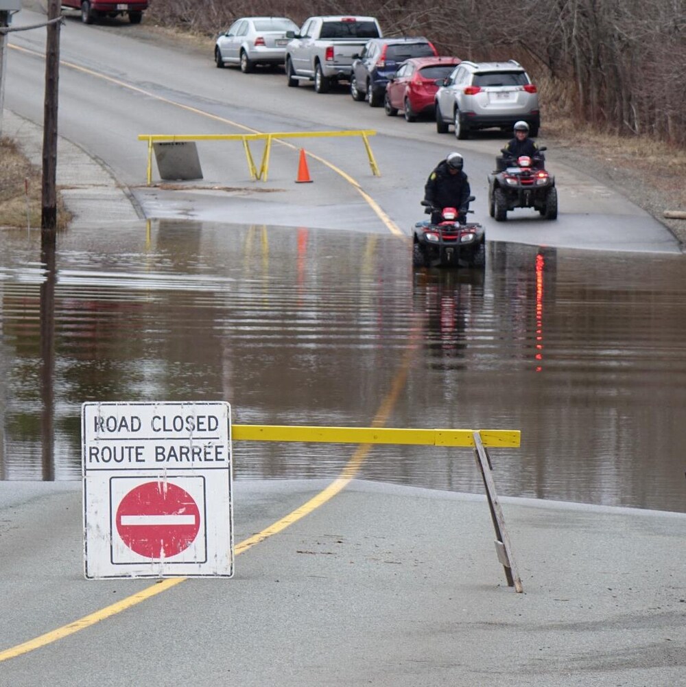 Deux personnes en VTT traversent une section de route inondée interdite à la circulation.