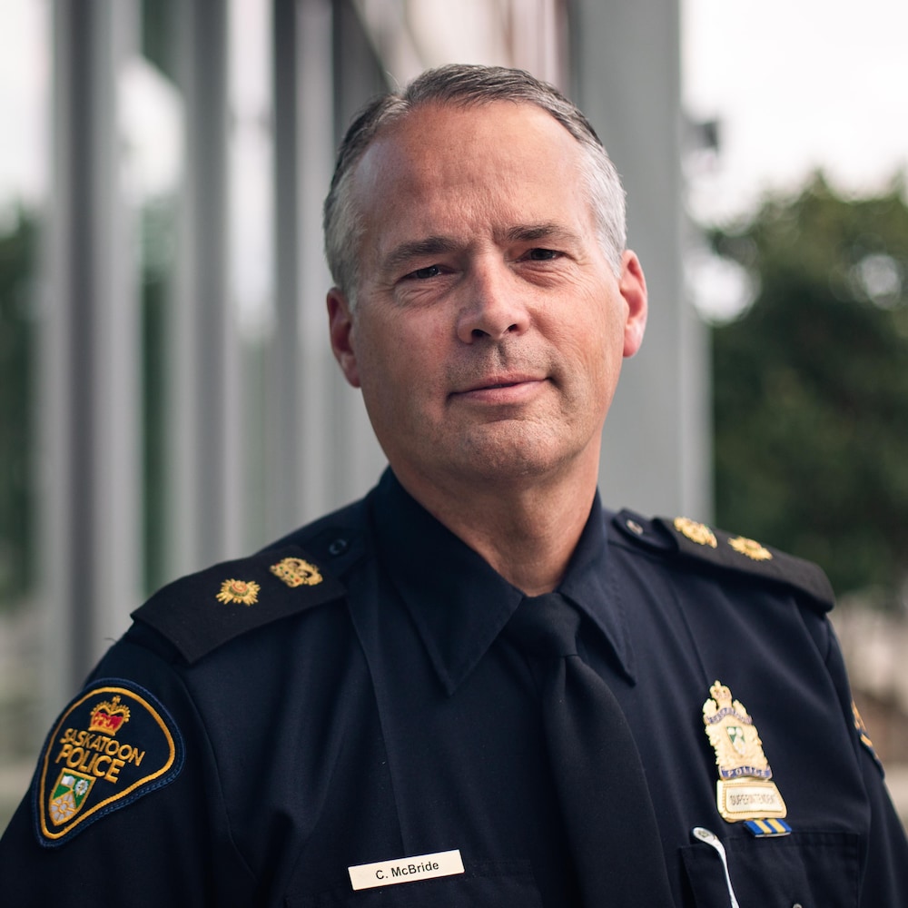 Le chef du Service de Police de Saskatoon, vêtu de son uniforme, regarde droit vers la caméra en souriant légèrement. 