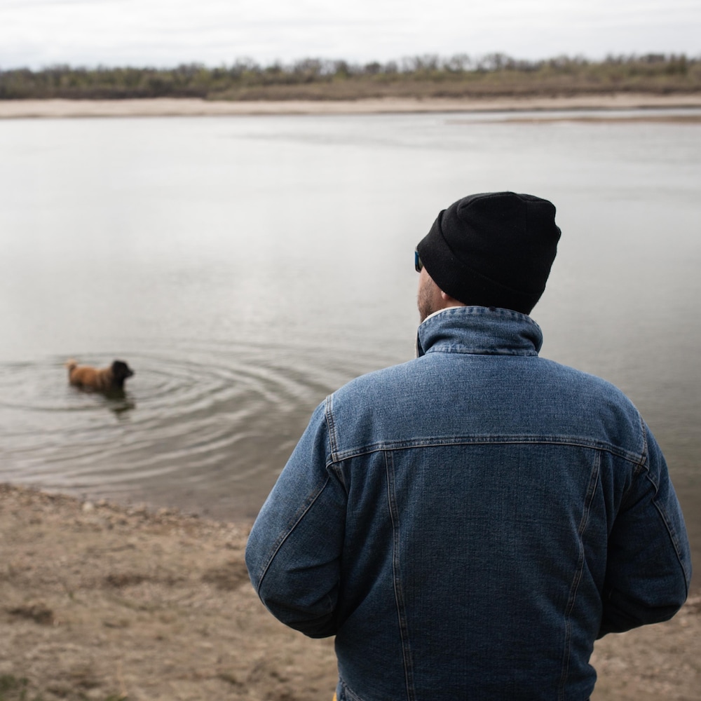 Jason, face au lac, regarde vers l'horizon pendant que son chien nage.