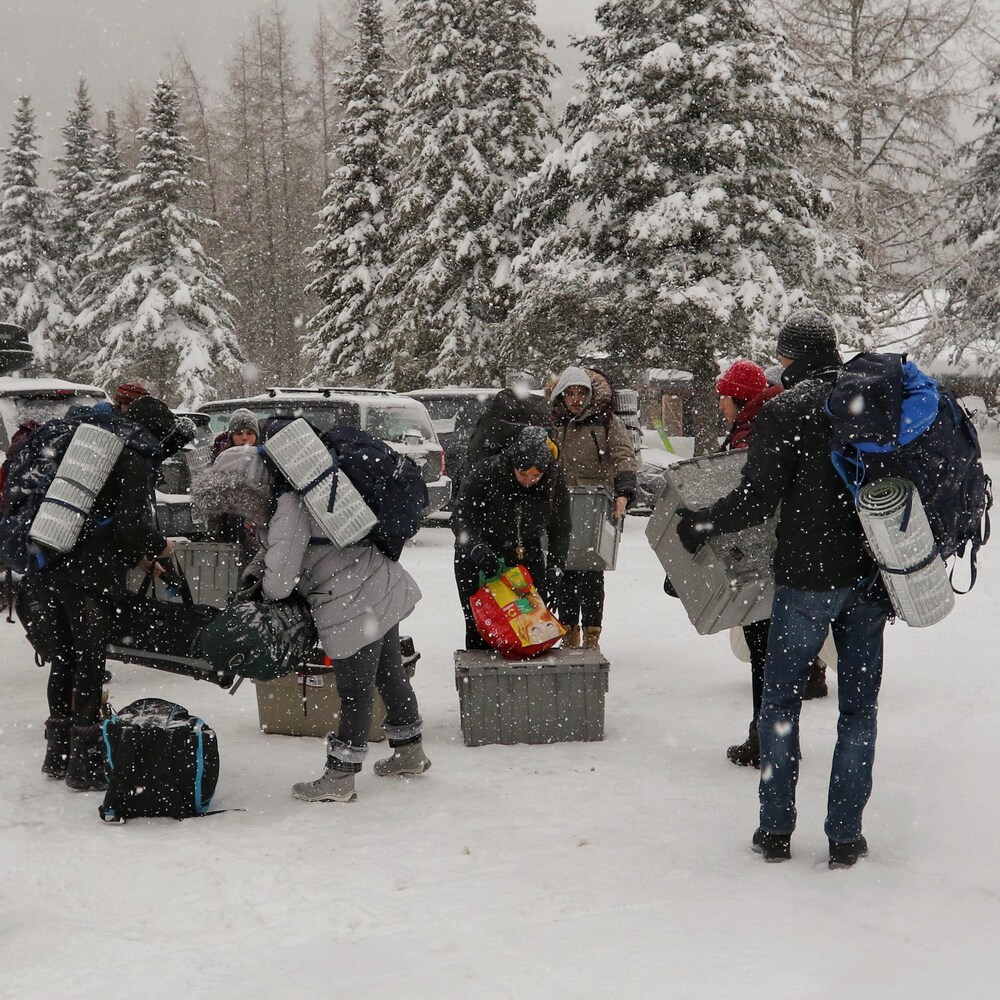 Des jeunes transportent des sacs dos et des boîtes de plastique. Un paysage hivernale les entoure.