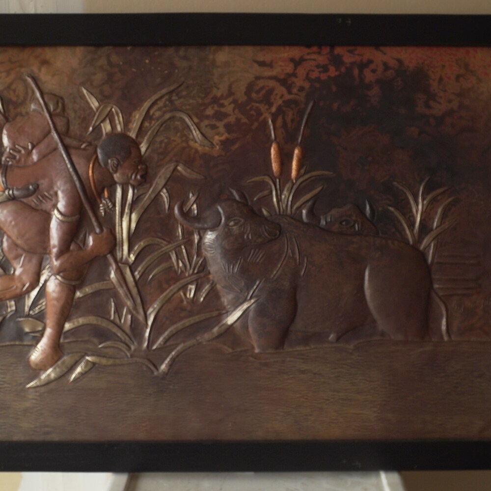 Un tableau en cuivre martelé qui représente un chasseur congolais qui s'approche d'un buffle sauvage.