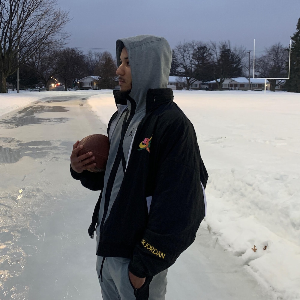 Un jeune homme debout dans un parc l'hiver tient un ballon de football dans ses mains.