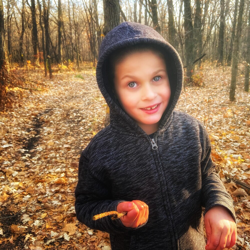 Justin sourit a la caméra. La photo est prise dans un boisé, et c'est l'automne.