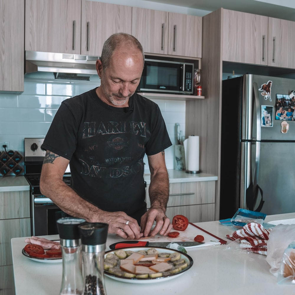 Denis est dans une cuisine en train de cuisiner, devant lui une assiette pleine de nourriture coupée, bien arrangée, en octobre 2022, à Edmonton, en Alberta.