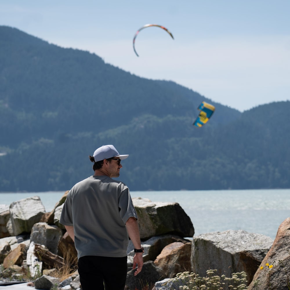 Olivier Corbeil en train de marcher proche de l'estuaire de Squamish, en arrière-plan des personnes font du kitesurf, en Colombie-Britannique, en juillet 2026.