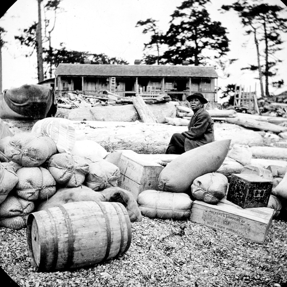 Photo d'archive datant de 1895, un homme atteint de la maladie de Hansen est assis sur des sacs et coffres de vivres déposés à même le sol sur l'île d'Arcy en Colombie-Britannique.