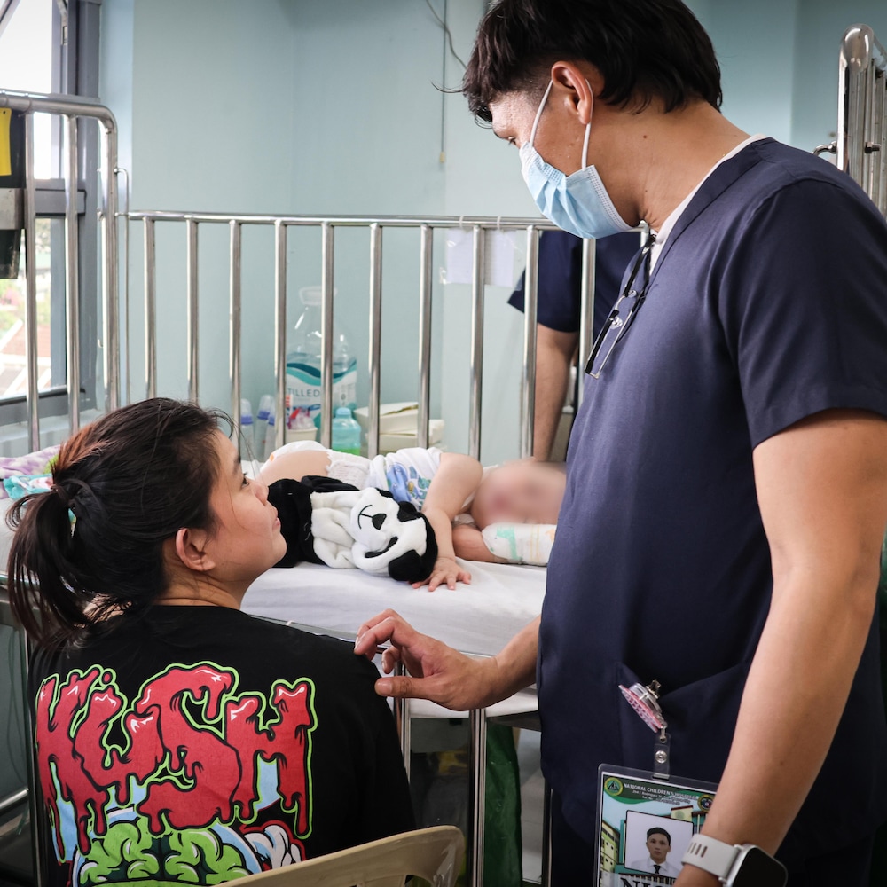 Nicolito Oba à l'hôpital en train de parler a une proche d'un bébé allongé sur un lit d'hôpital, à Manille, aux Philippines, en mai 2025.