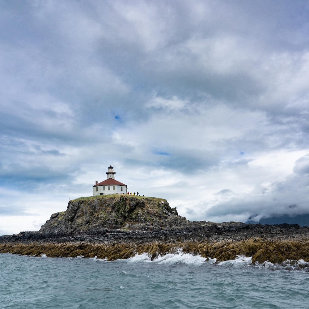 Le phare d'Eldred Rock se dresse en haut de son rocher dans le canal Lynn avec des montagnes dans le fond et l'océan, en Alaska, juillet 2022.