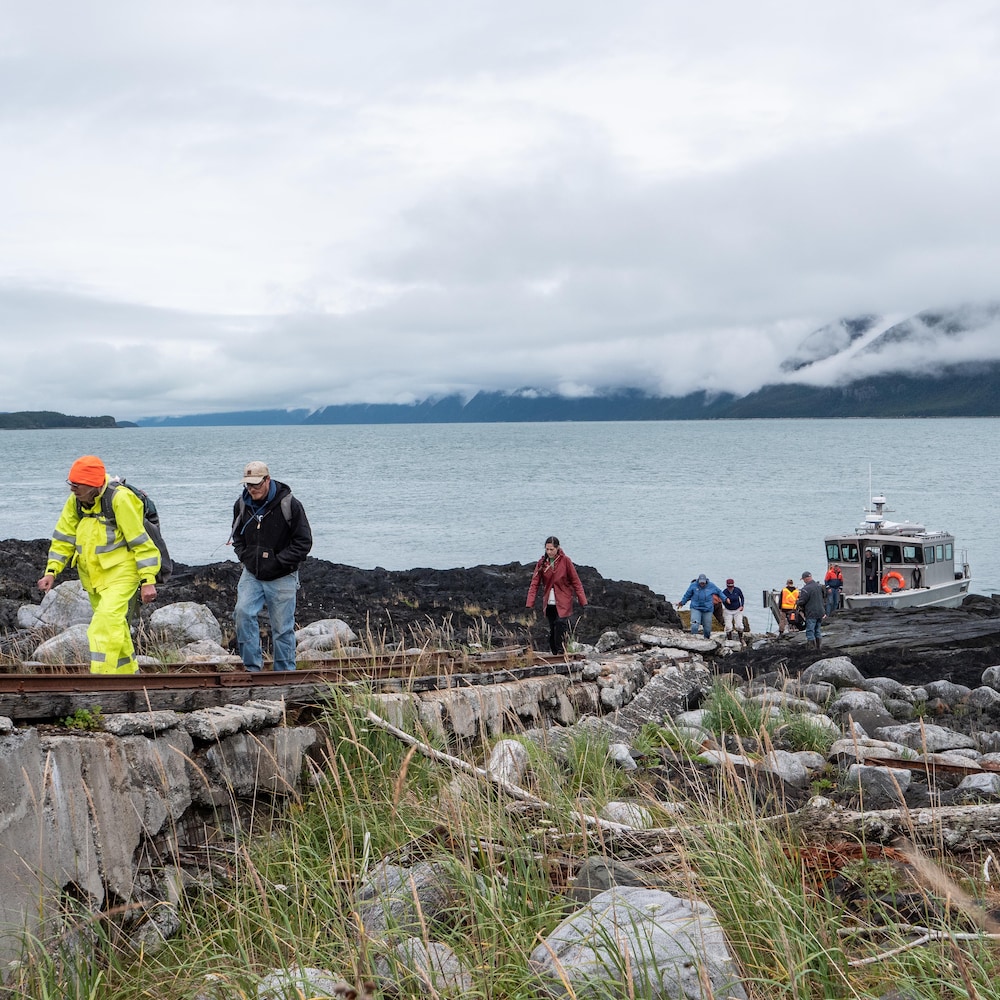 Un groupe de personne débarque d'un petit bateau de pêche, au fond l'océan et la côte, en Alaska, juillet 2022.