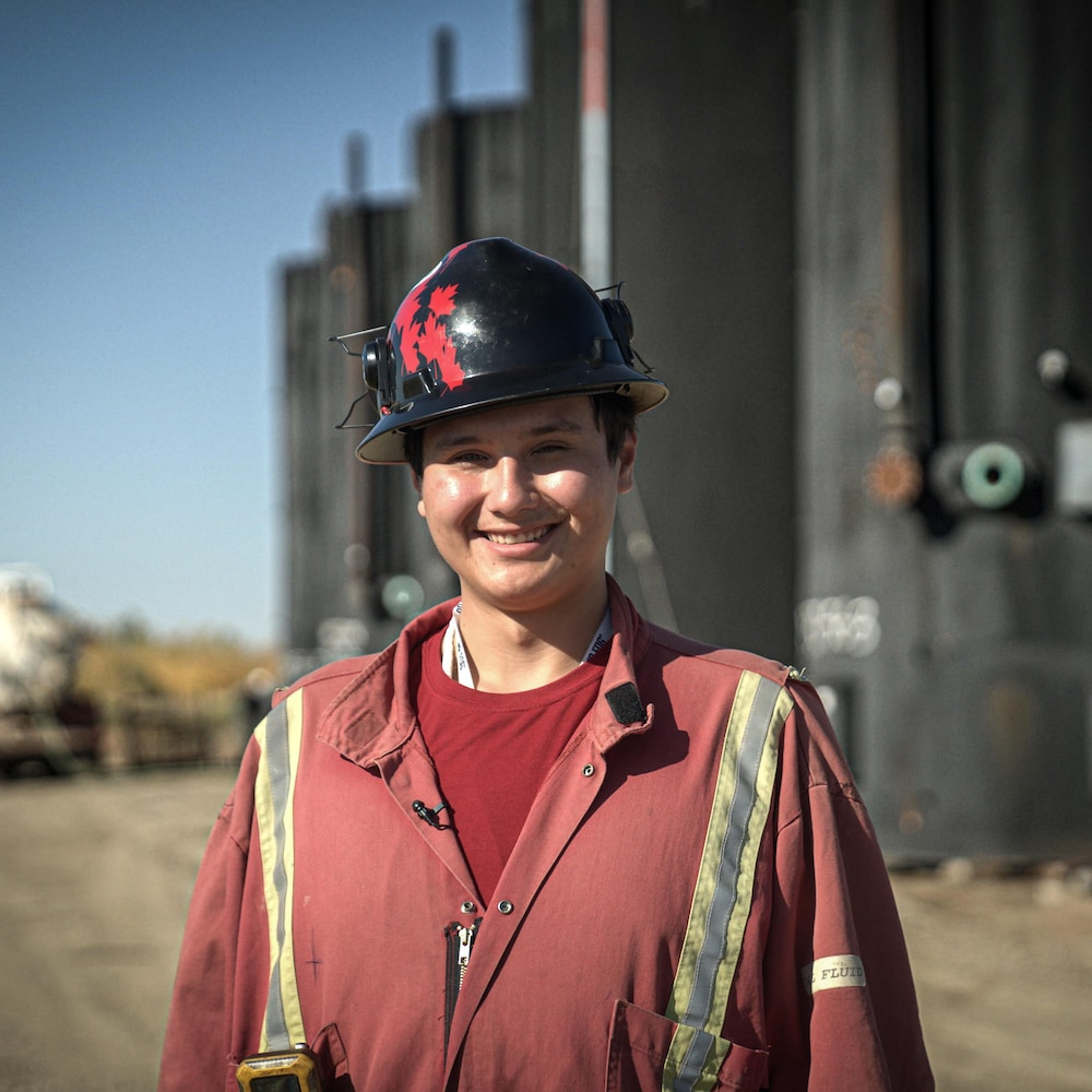 Drayshawn Stanley in work clothes and hat in front of abandoned oil wells in Frog Lake in October 2022.