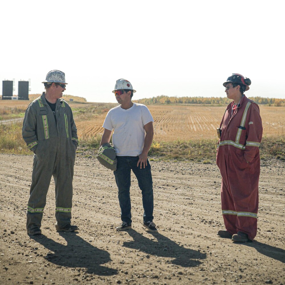 Kevin Heck, Joshua Abrahams et Drayshawn Stanley en train de discuter debout sur un chemin de terre devant un champ près de Frog Lake, en Alberta, en ocotobre 2022.                    