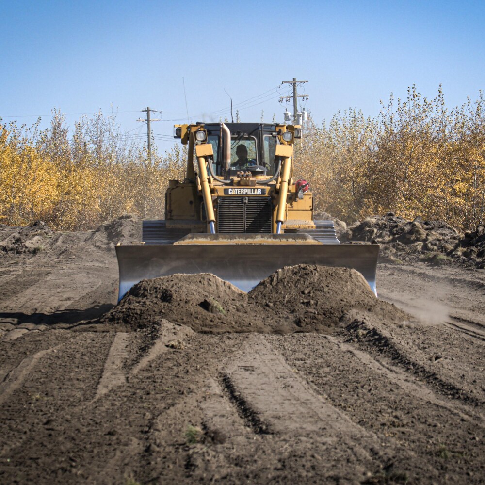 A tractor plows the soil with a backhoe against a backdrop of small trees in the Alberta prairie near Frog Lake in October 2022.      