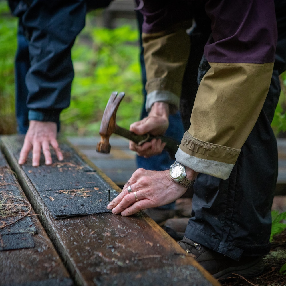 Nowell Senior et Mikel Leclerc sont en train de clouer de l'antidérapant sur des planches au sol dans la forêt du parc Chun T'oh Whudujut, en Colombie-Britannique, en juin 2022.