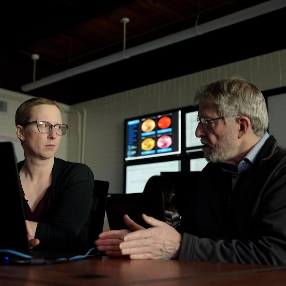 Les chercheurs Robyn Fiori et David Boteler assis à une table, en train de discuter, au Centre canadien de météo spatiale, près de Saskatoon, en février 2024.