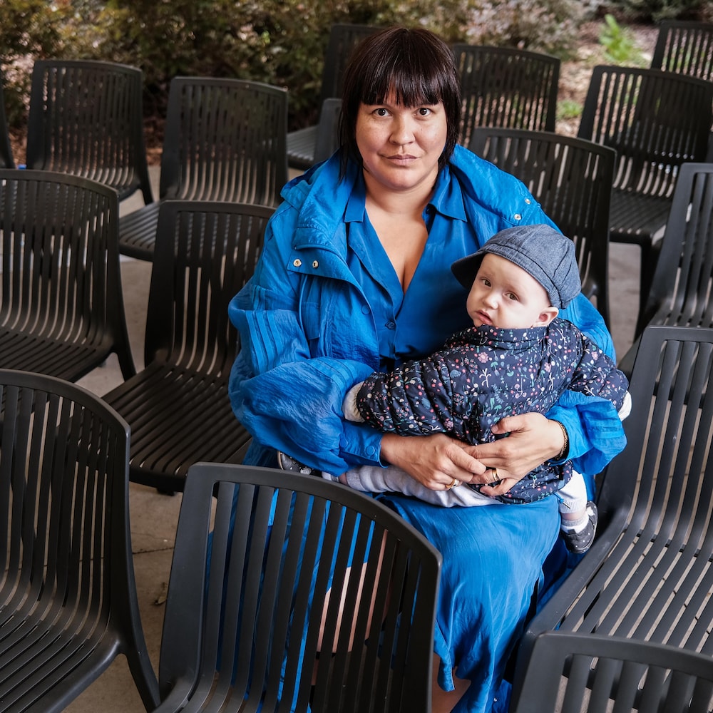 Swaneige Bertrand est assise sur une chaise parmis d'autre, tenant un bébé dans les bras, au Jardin botanique de Montréal, en août 2022.