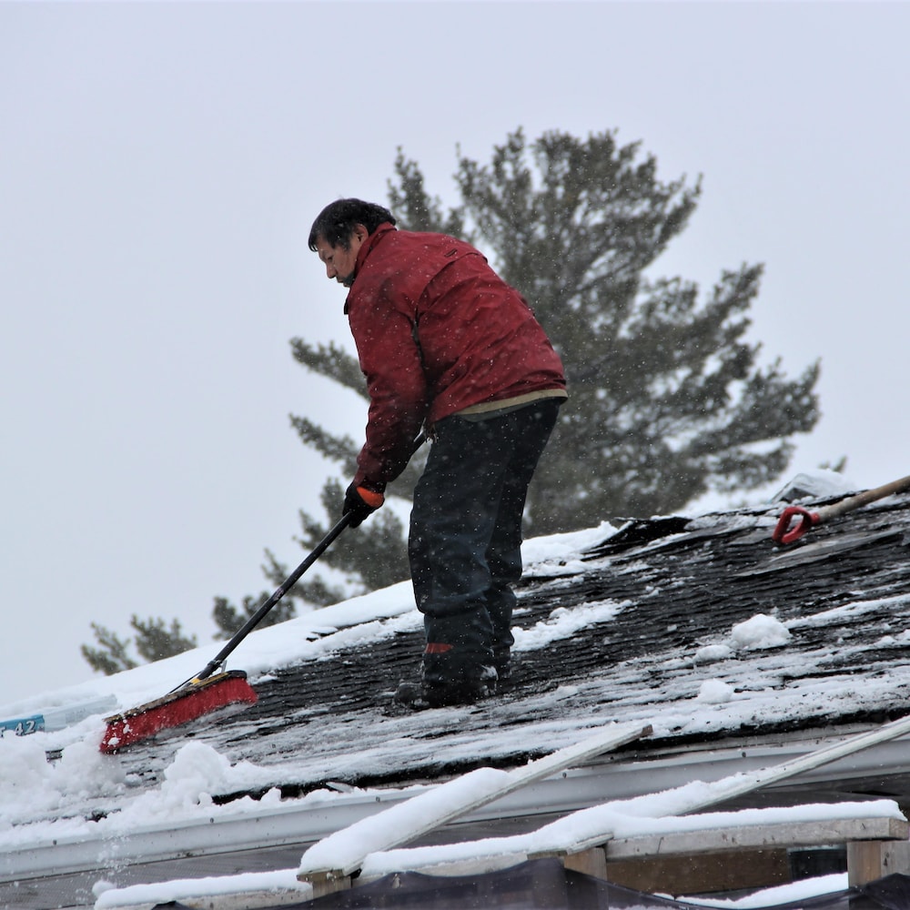Un homme sur un toit enlève la neige avec un balai. 