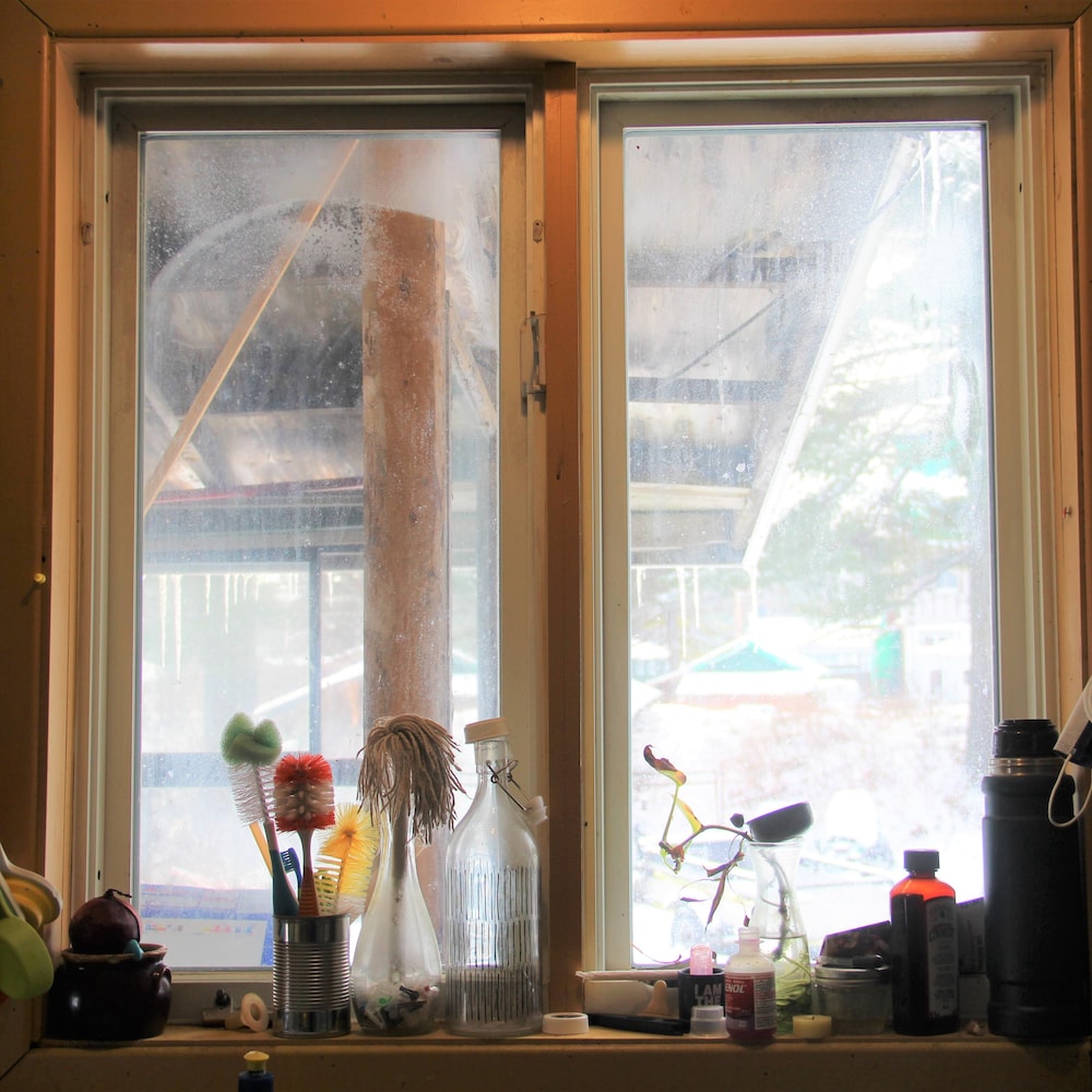 Vue d'une fenêtre de cuisine avec des ustensiles déposés sur une tablette et accrochés au mur.