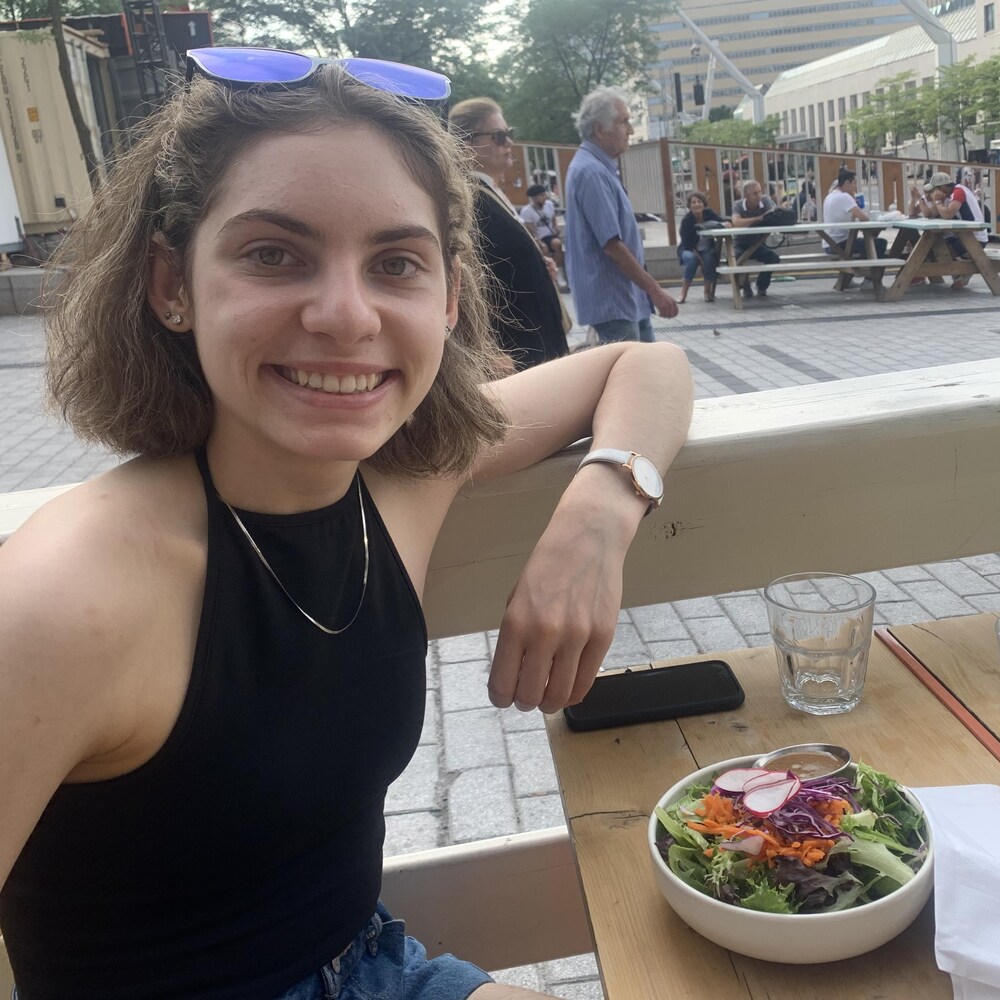 Simone, souriante, est assise à la terrasse d'un restaurant devant un bol de salade.