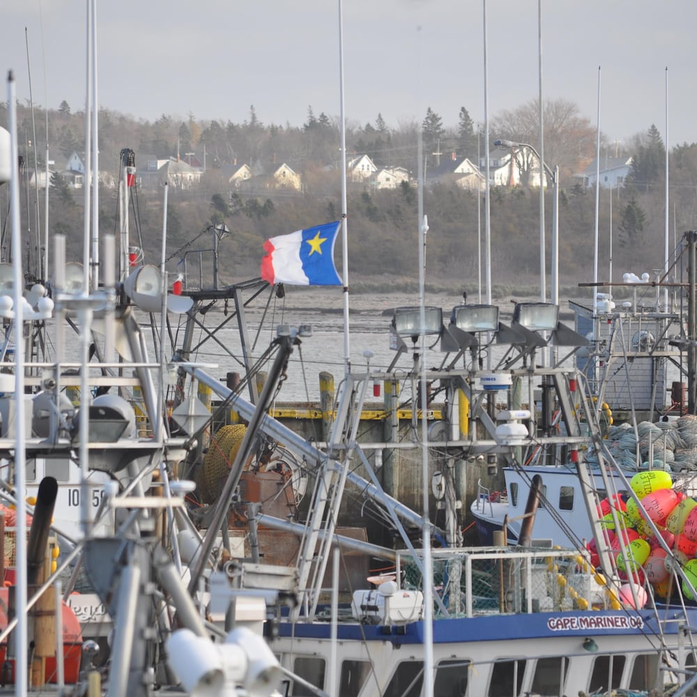 Un drapeau acadien flotte accroché sur le mat d'un bateau de pêche.