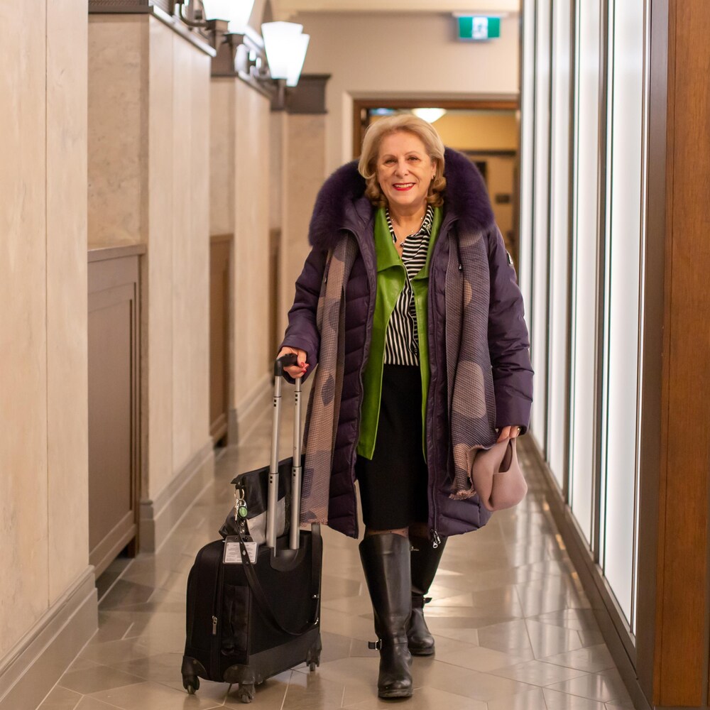 La députée avec son manteau et sa valise sur roulettes dans un corridor du parlement temporaire à Ottawa.