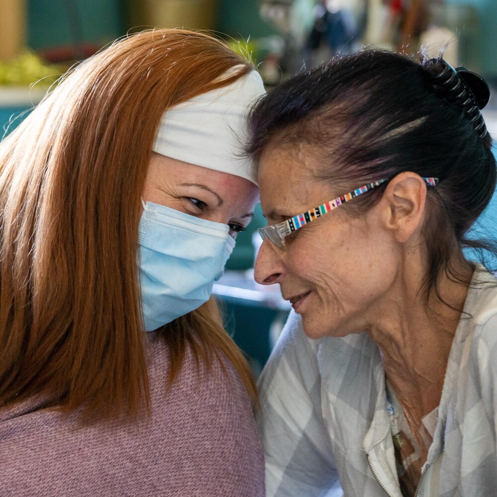 Une infirmière masquée appuie son front sur celui de sa patiente en souriant.