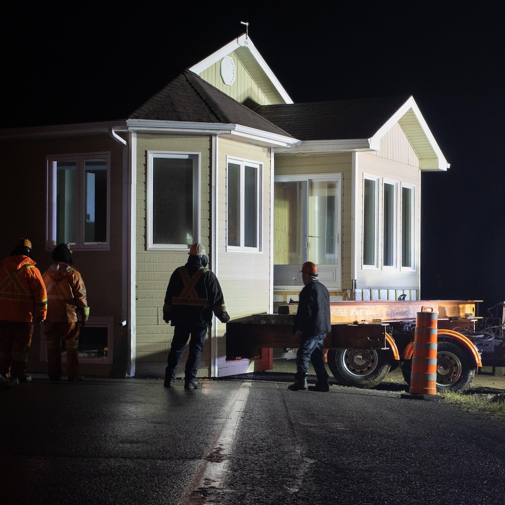 Des travailleurs observent une maison en travers d'une route, la nuit.