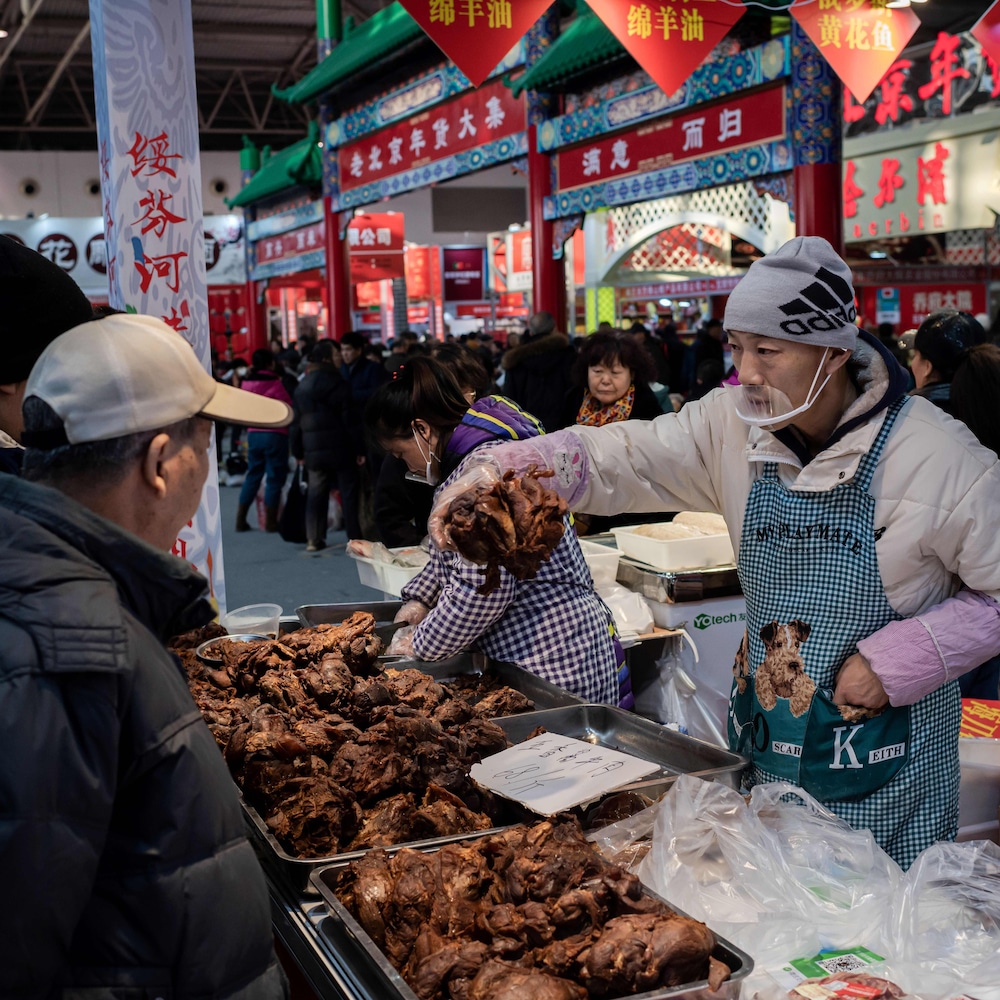 Un homme tient de la viande dans sa main pour le montrer à un client. Il y a foule dans ce marché.