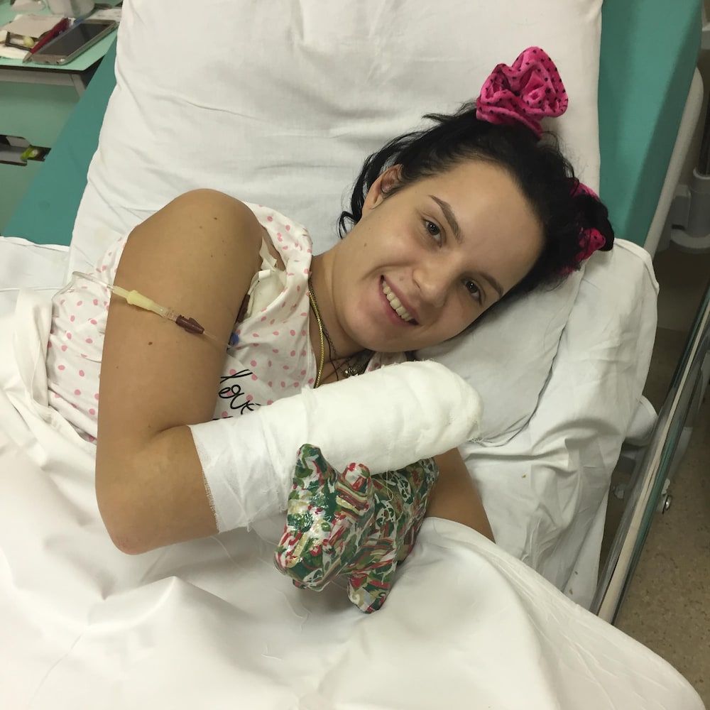 Margarita Gracheva est étendue sur un lit d'hôpital, souriante. Un de ses avant-bras est complètement couvert de bandage et l'autre est caché sous le drap.