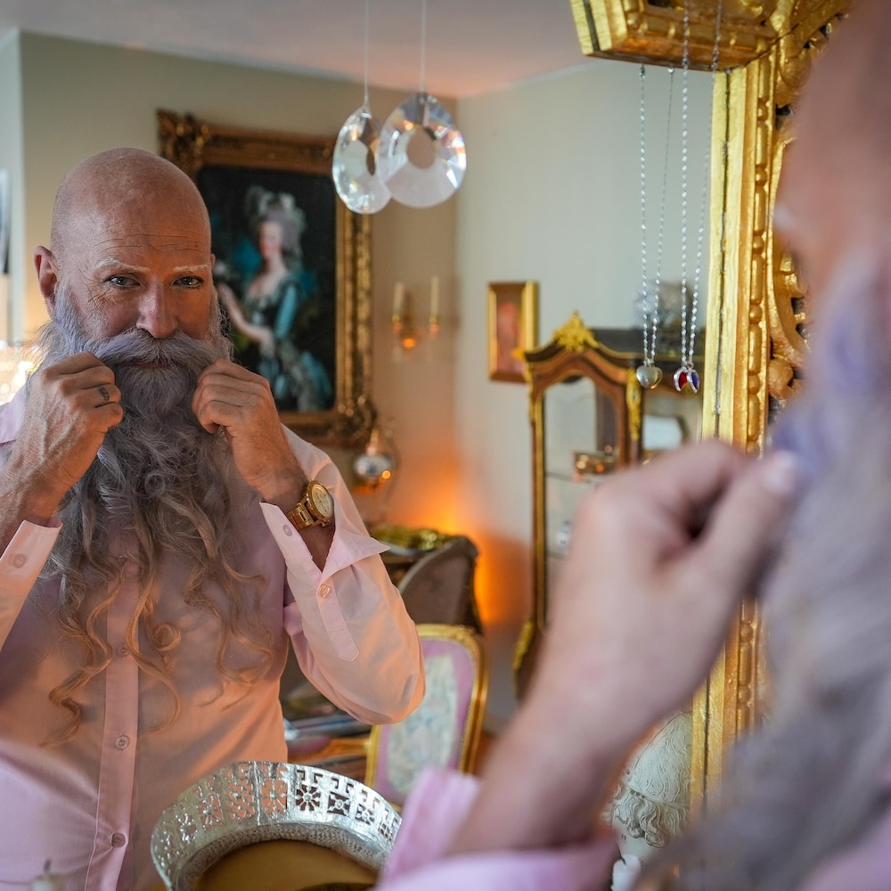 Mark Henderson se regarde et coiffe sa barbe dans un miroir doré.