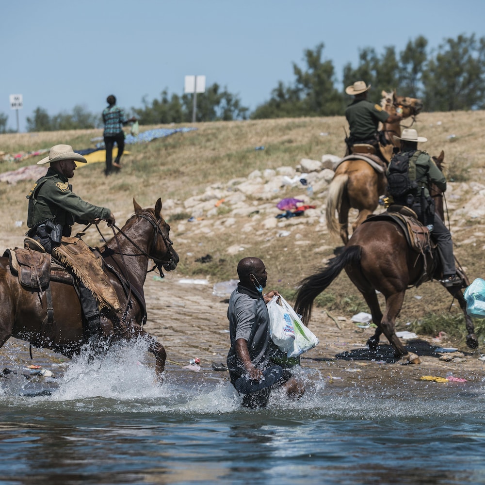 Des cavaliers américains sont dans le Rio Grande avec leurs chevaux et poursuivent des Haïtiens qui essaient de sortir de l'eau.