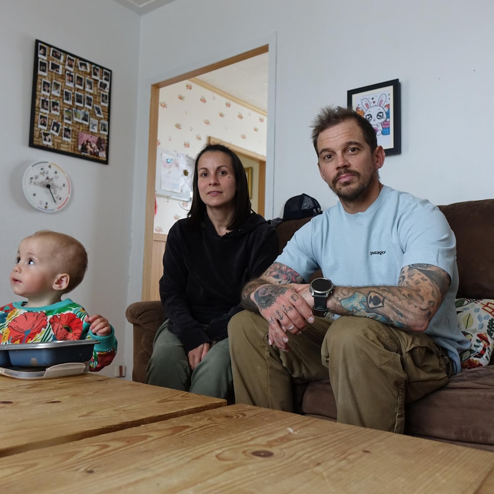 Un couple dans la trentaine est assis dans le salon avec un jeune enfant debout devant eux. 