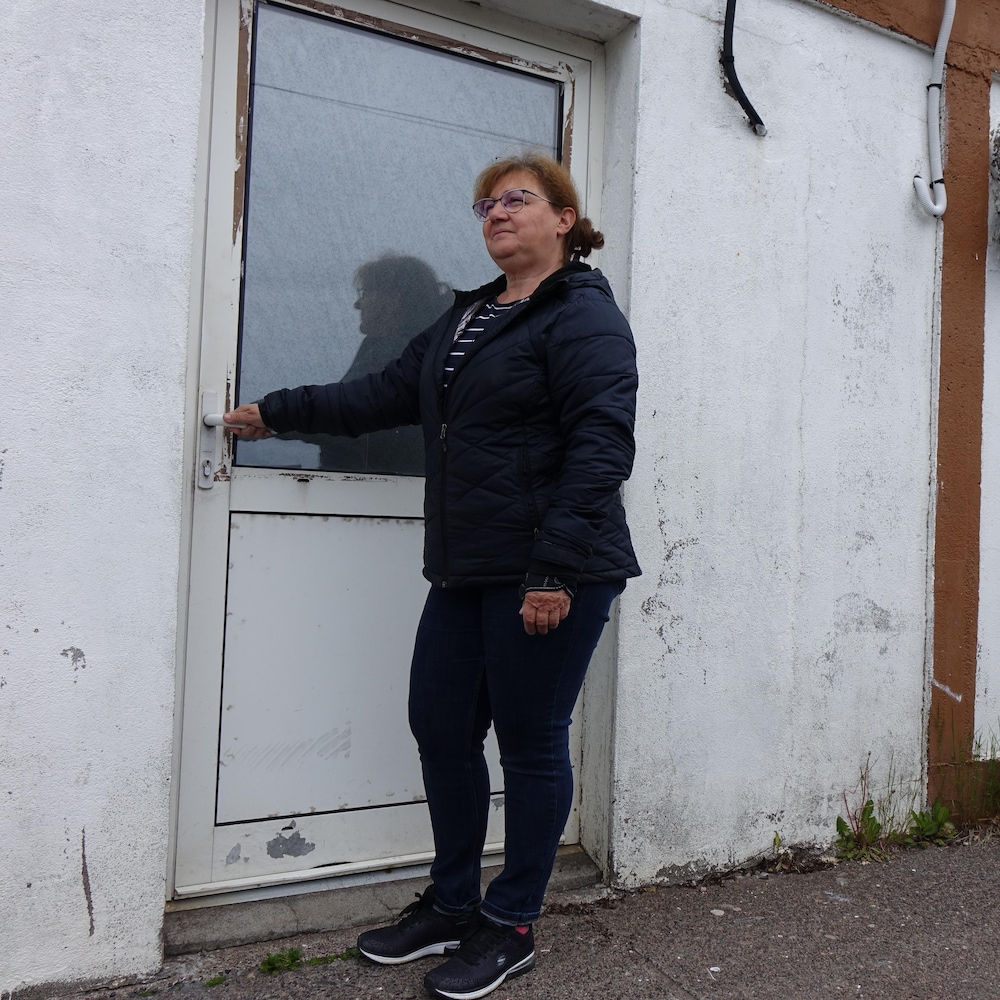 Une femme est devant un bâtiment et tient la poignée de la porte. 