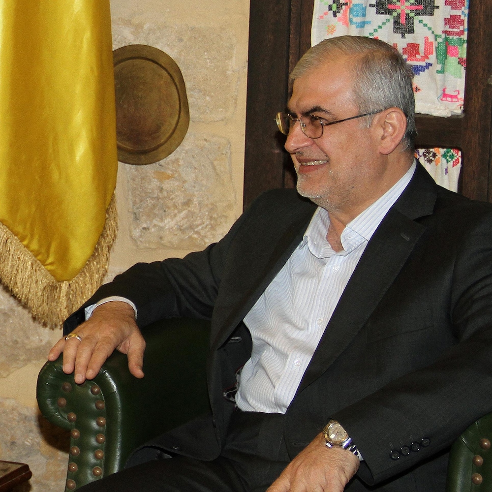 Deux hommes assis dans des fauteuils en cuir vert foncé, séparés par les drapeaux du Liban, de la Russie et du Hezbollah.