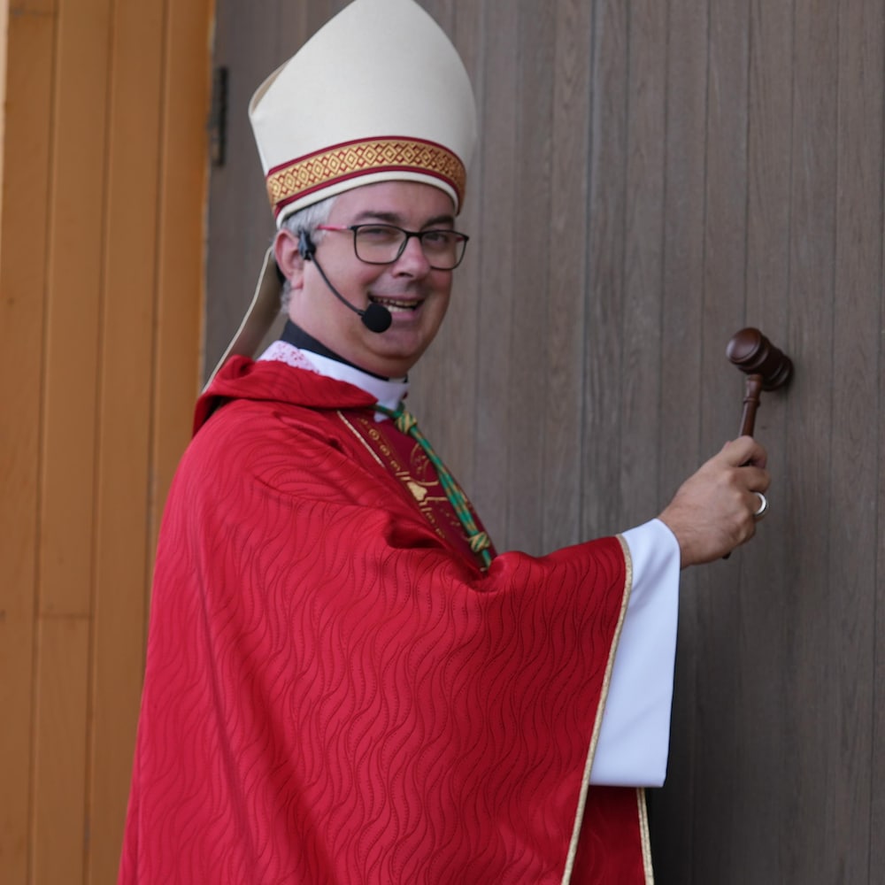 Monseigneur Pierre-Olivier Tremblay frappe sur la porte de la cathédrale avec un maillet.
