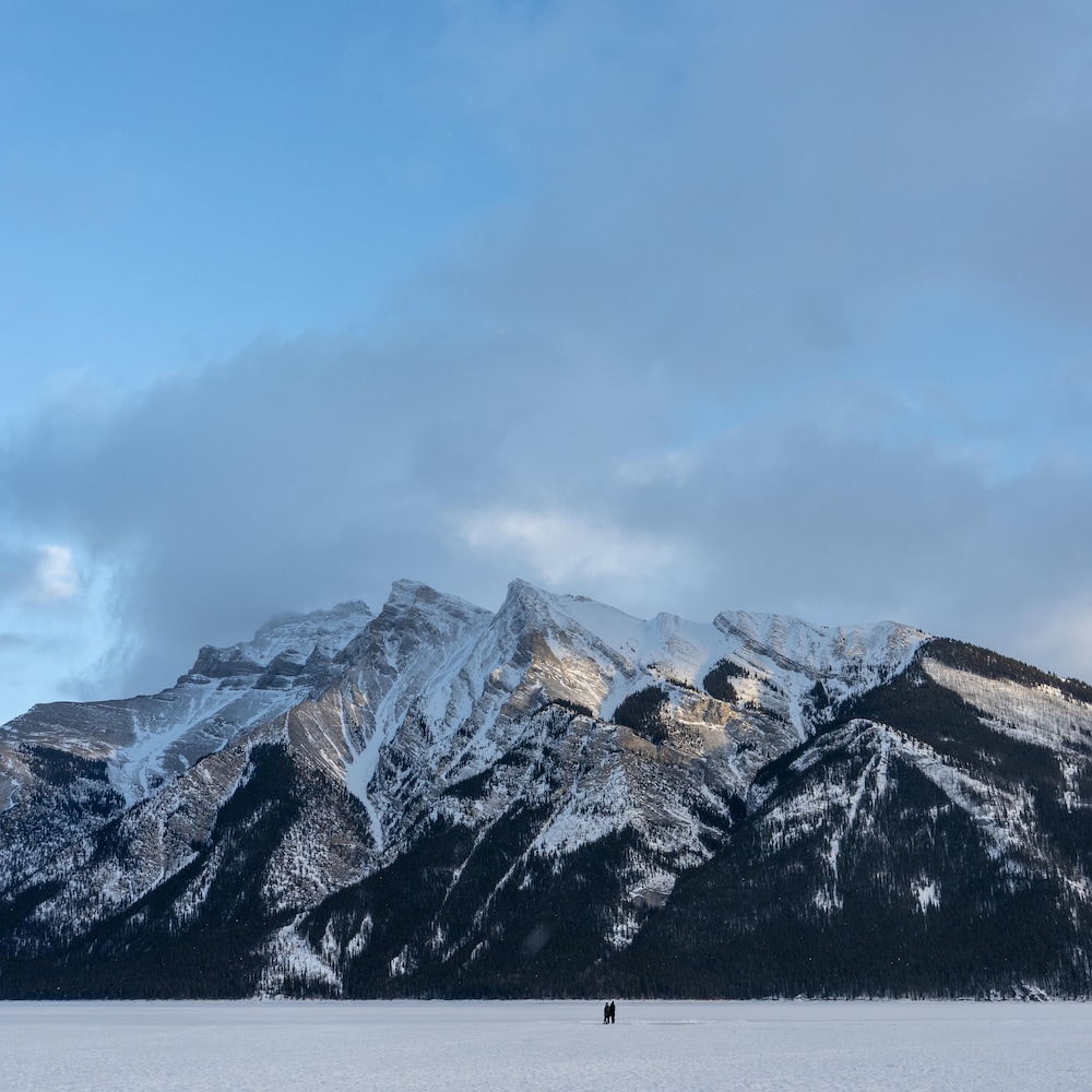 Deux personnes vues de loin, sur un lac gelé, avec des montagnes en arrière plan. 