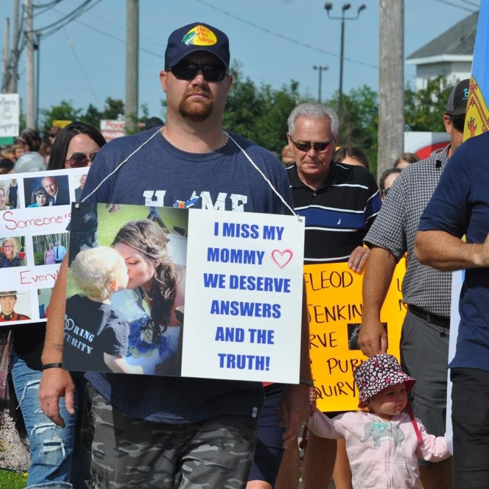 Un homme marche en tenant une affiche sur laquelle on peut lire : I miss my mommy we deserve answers and the truth!