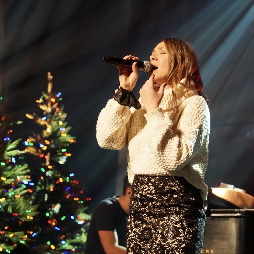 Une chanteuse en tricot blanc chante devant un décor de Noël.
