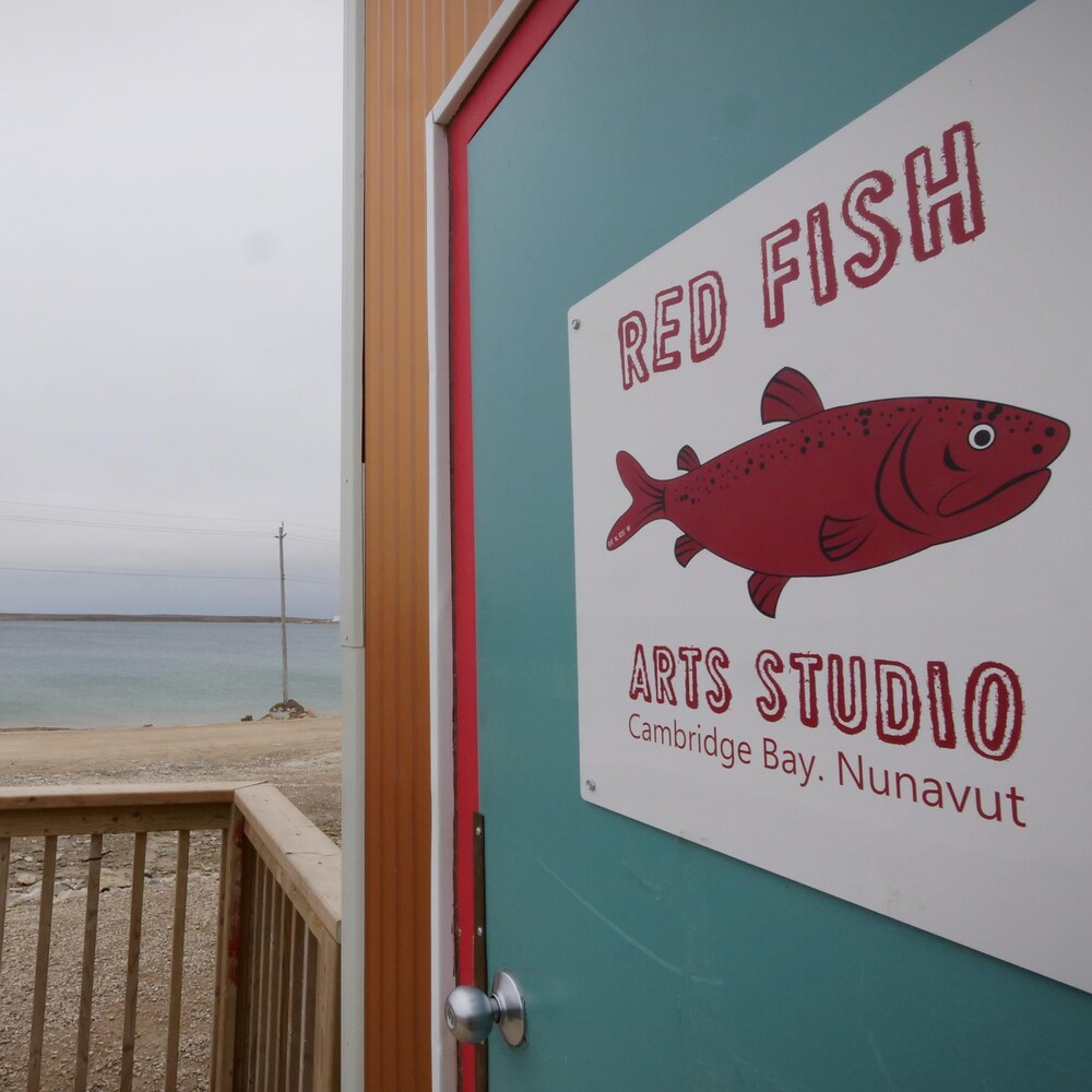 La façade du studio Red Fish Arts de Cambridge Bay, avec un bâteau à l'arrière-plan.