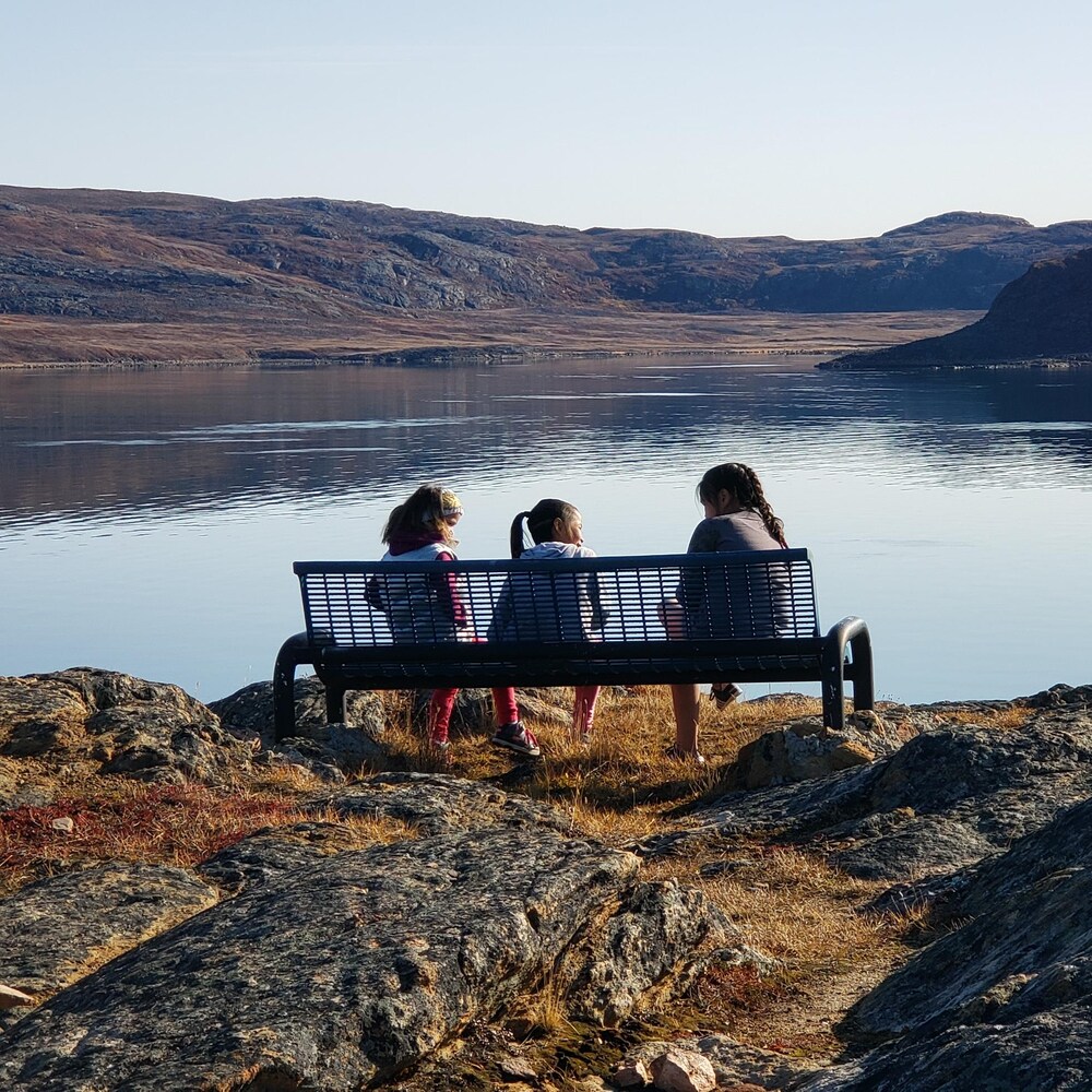 Trois jeunes filles sont assises sur un banc, devant un vue montagneuse, en septembre 2019.