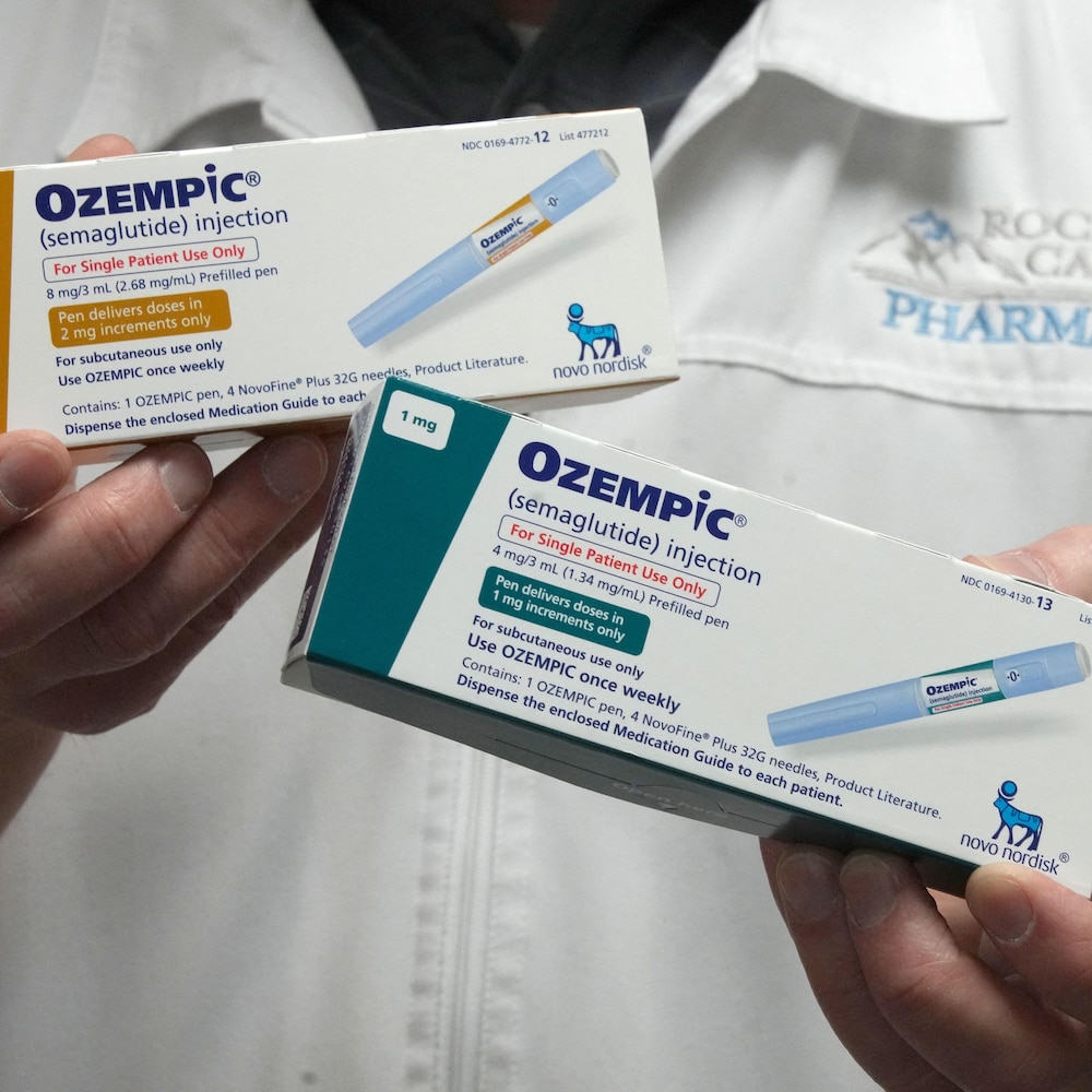 Un homme vêtu d'un sarrau de pharmacien tient dans ses mains deux boîtes d'Ozempic, qui affichent des informations sur le médicament et une photo d'un injecteur.