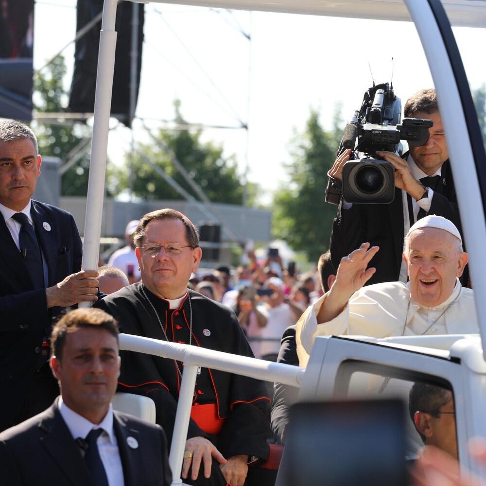 Les deux hommes souriant assis dans la papemobile. Le pape envoie la main à la foule.