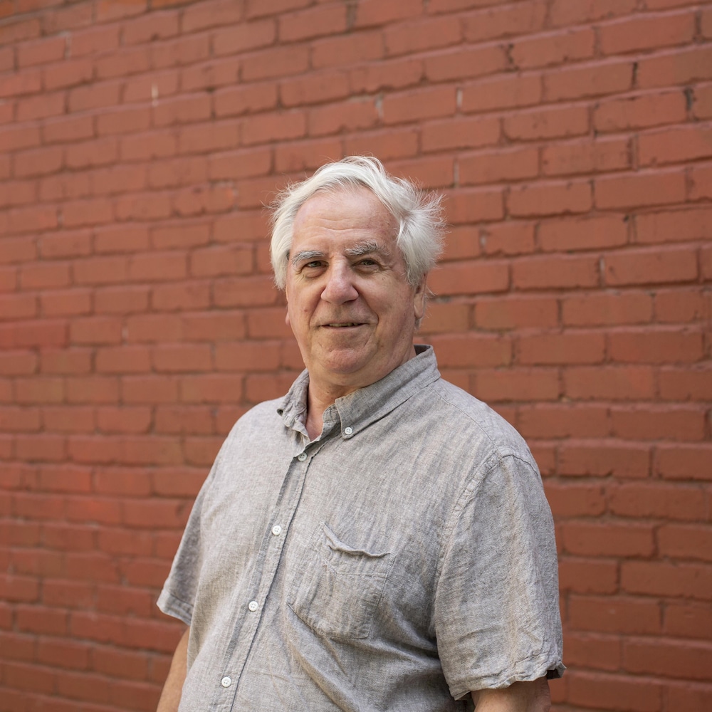 Portrait de Gérard Beaudet, professeur titulaire à l'école d'urbanisme et d'architecture de paysage de l'Université de Montréal, devant un mur de briques.