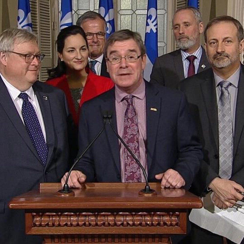 Le président du syndicat des professionnels du gouvernement du Québec entouré de députés de l'opposition dans le foyer du parlement.