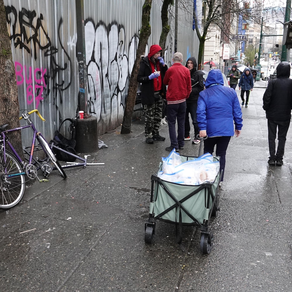 Une femme se promène sur le trottoir d'une rue passant avec un chariot contenant des repas individuels.