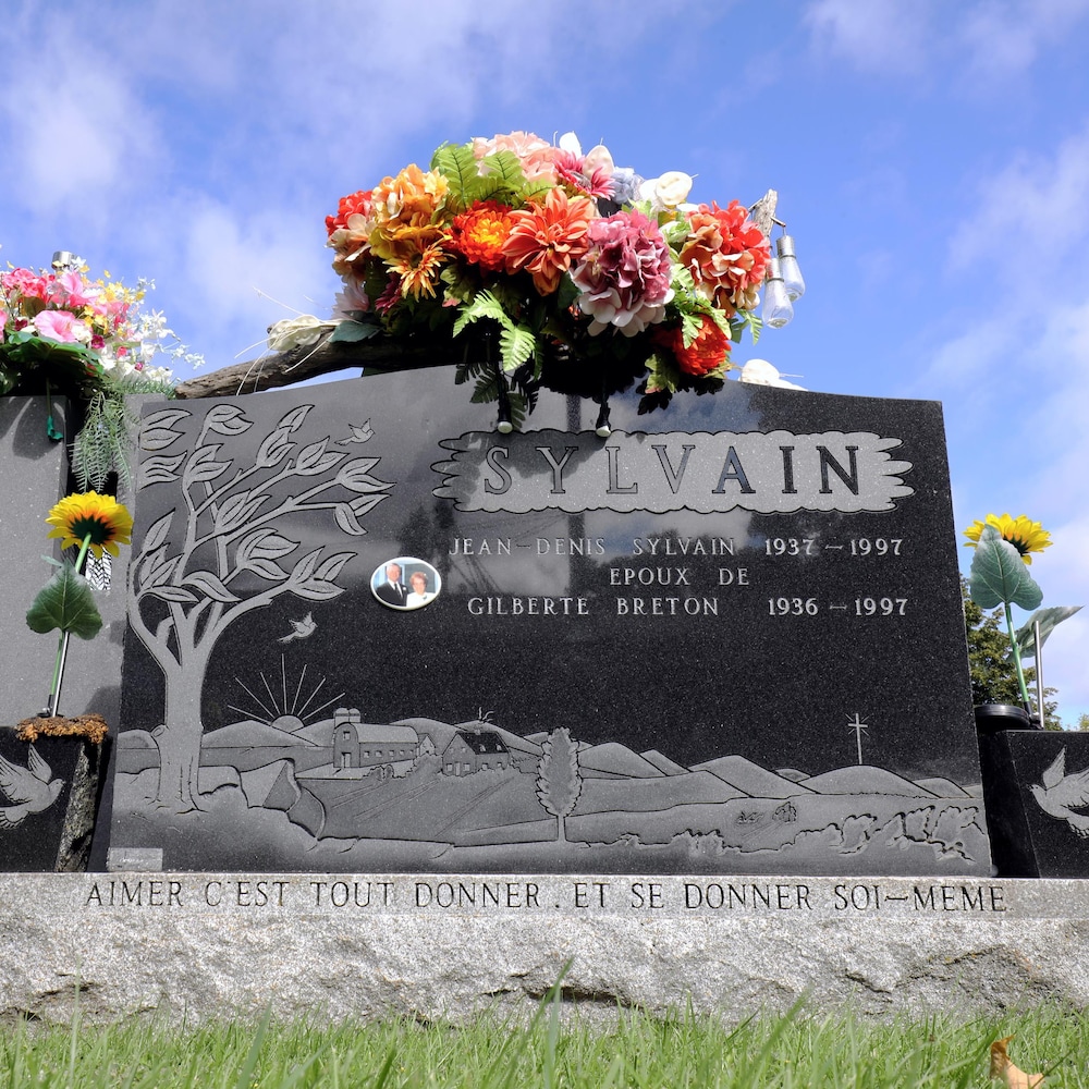 La pierre tombale de Jean-Denis Sylvain et Gilberte Breton. Le dessin sur la pierre montre une ferme et il est inscrit : «Aimer c'est tout donner. Et se donner ssoi-même».