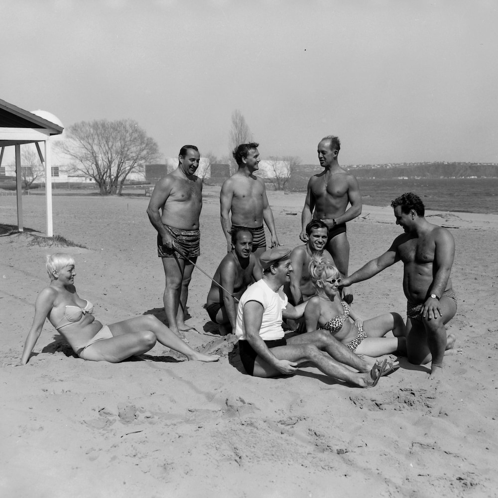 Un groupe de baigneurs détendus, dans les années 1960. Le soleil plombe mais la plage semble déserte.