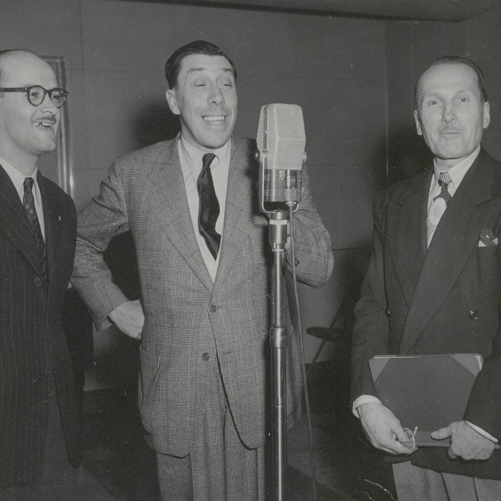 Fernandel dans un studio de CBJ devant un micro sur pied. Vilmont Fortin et un autre homme sont à ses côtés.